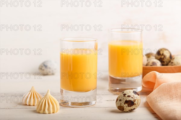 Sweet egg liqueur in glass with quail eggs and meringues on white wooden background. Side view,