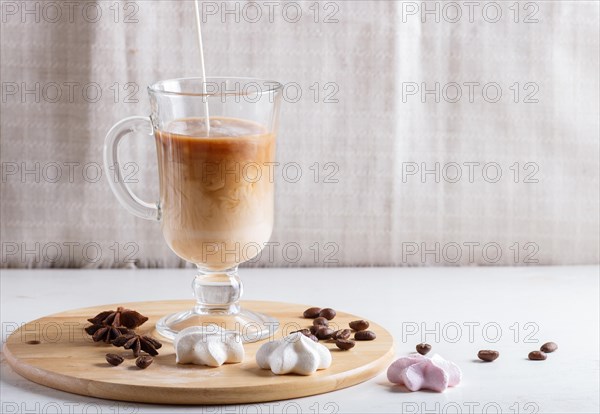Glass cup of coffee with cream poured over and meringues on a wooden board on a white background.