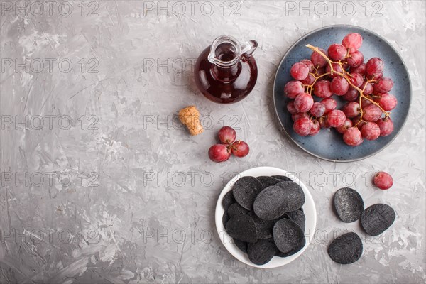 Black potato chips with charcoal, balsamic vinegar in glass, red grapes on a blue ceramic plate on