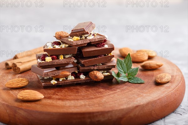 A pieces of milk chocolate with almonds and dried fruits on a brown wooden board on a gray concrete