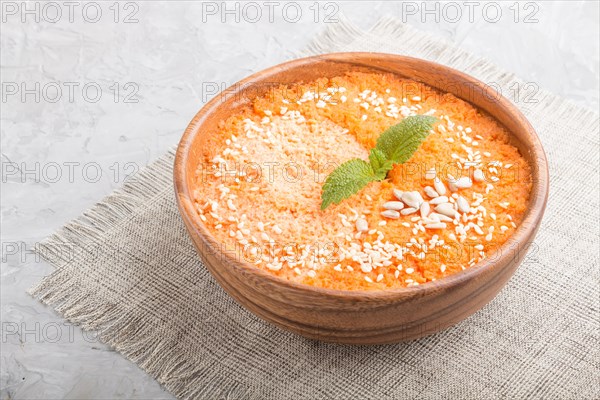 Carrot cream soup with sesame seeds in wooden bowl on a gray concrete background with linen textile