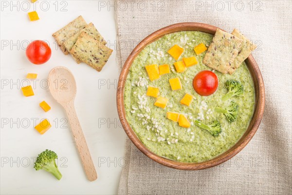 Green broccoli cream soup with crackers and cheese in wooden bowl on a white wooden background and