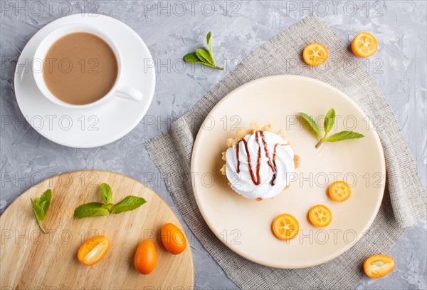 Cake with whipped egg cream on a light brown plate with kumquat slices and mint leaves on a gray