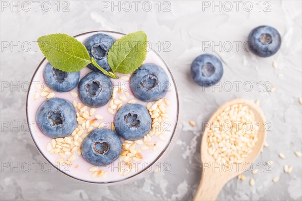 Yoghurt with blueberry and sesame in a glass and wooden spoon on gray concrete background. top