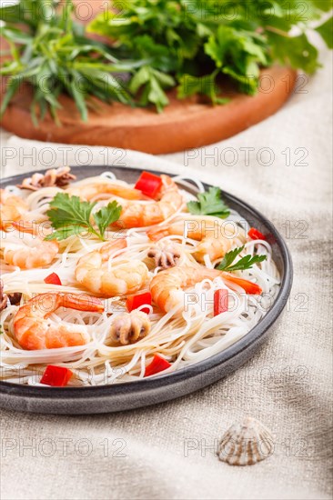 Rice noodles with shrimps or prawns and small octopuses on gray ceramic plate on a white linen