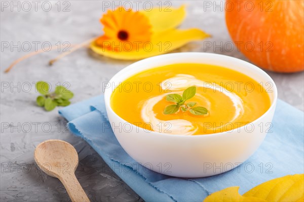 Traditional pumpkin cream soup with in white bowl on a gray concrete background with blue napkin.