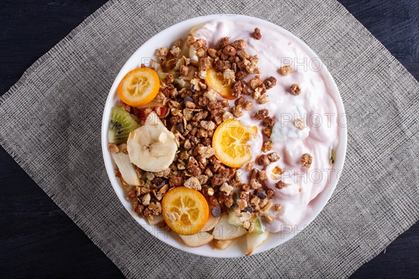 Vegetarian salad of bananas, apples, pears, kumquats, kiwi with granola and yogurt on black woodem