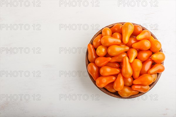 Fresh orange grape tomatoes in wooden bowl on white wooden background. top view, flat lay, copy