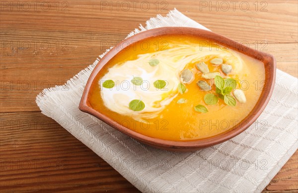 Traditional pumpkin cream soup with seeds in clay bowl on a brown wooden background with linen
