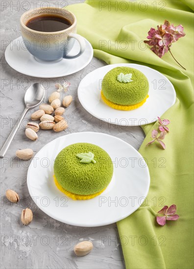 Green mousse cake with pistachio cream and a cup of coffee on a gray concrete background and green