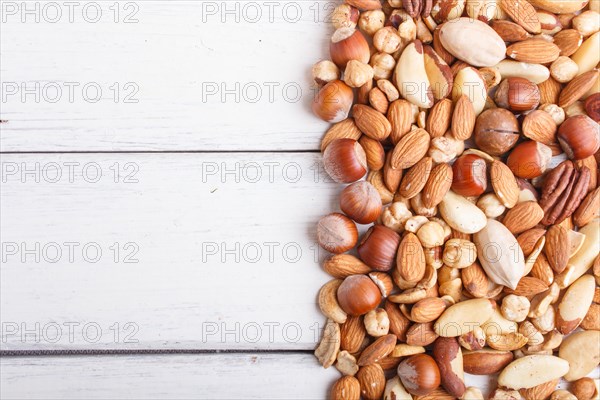 Mixed different kinds of nuts on white wooden background. hazelnut, brazil nut, almond, pumpkin