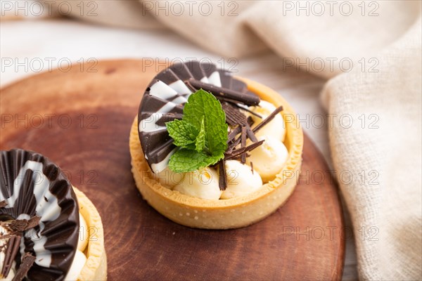 Sweet tartlets with chocolate and cheese cream with cup of coffee on a white wooden background and