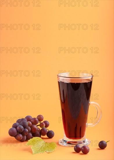Glass of red grape juice on orange background. Morninig, spring, healthy drink concept. Side view,