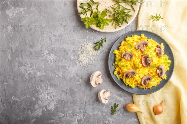 Yellow fried rice with champignons mushrooms, turmeric and oregano on blue ceramic plate on a gray