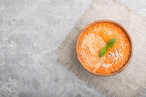 Carrot cream soup with sesame seeds in wooden bowl on a gray concrete background with linen textile