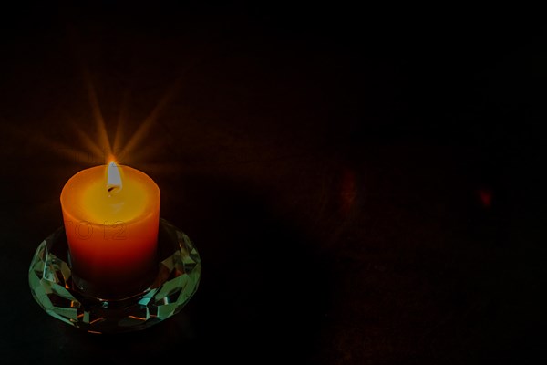 Burning candle in glass holder isolated on black textured background. Small amount of grain added