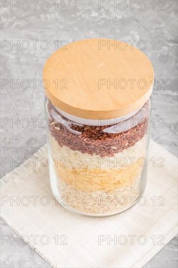 Glass jar with different kinds of rice poured in layers on a gray concrete background. side view,