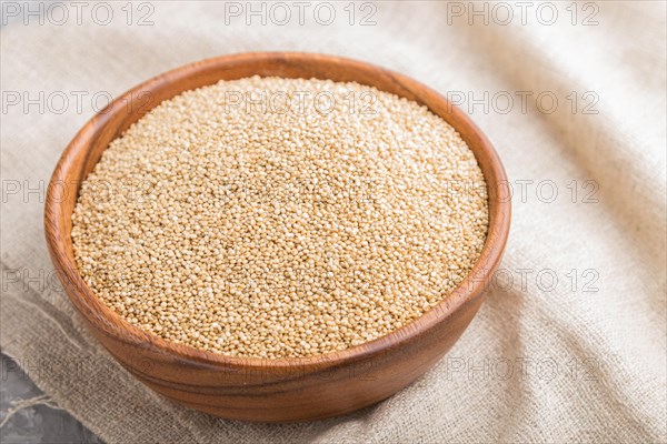 Wooden bowl with raw white quinoa seeds and wooden spoon on a gray concrete background and linen