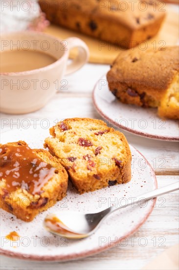 Homemade cake with raisins, almonds, soft caramel and a cup of coffee on a white wooden background.
