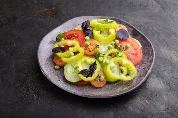 Vegetarian salad from green pea, tomatoes, pepper and basil on a black concrete background. Side