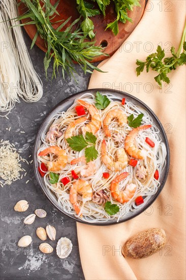 Rice noodles with shrimps or prawns and small octopuses on gray ceramic plate on a black concrete