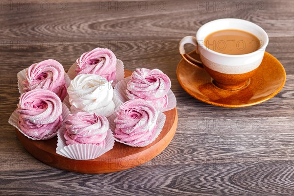 Pink and white marshmallows (zephyr) on a round wooden board with cup of coffee on a gray wooden