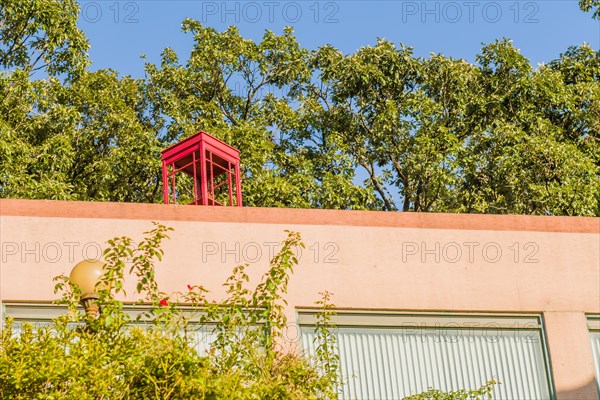 Red wooden telephone booth without glass on top of pink stucco building on sunny day with blue sky