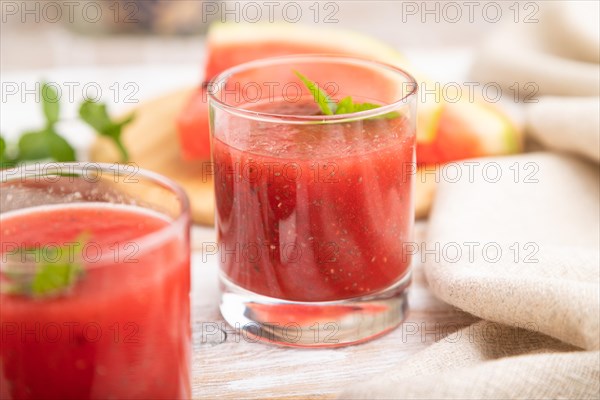 Watermelon juice with chia seeds and mint in glass on a white wooden background with linen textile.
