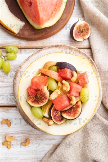 Vegetarian fruit salad of watermelon, grapes, figs, pear, orange, cashew on white wooden background