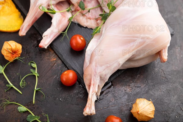 Whole raw rabbit with pumpkin, tomatoes, pea sprouts on a black concrete background and linen