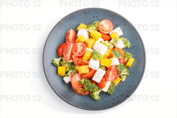 Vegetarian salad with broccoli, tomatoes, feta cheese, and pumpkin on a blue ceramic plate isolated