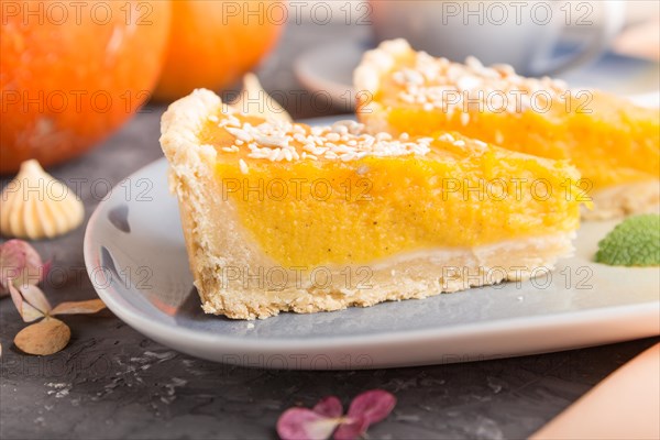 Two pieces of traditional american pumpkin pie with cup of coffee on a black concrete background