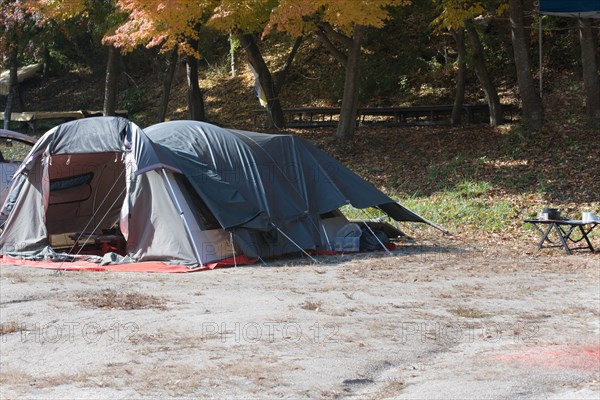 Camping tent set up in mountain park on sunny fall day with cooking pans on small wooden table in