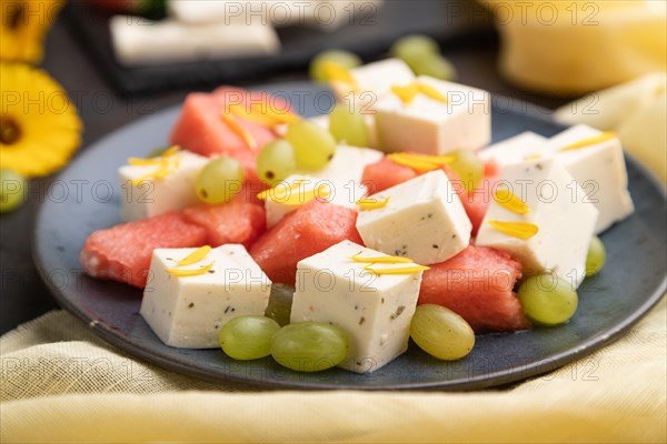 Vegetarian salad with watermelon, feta cheese, and grapes on blue ceramic plate on black concrete