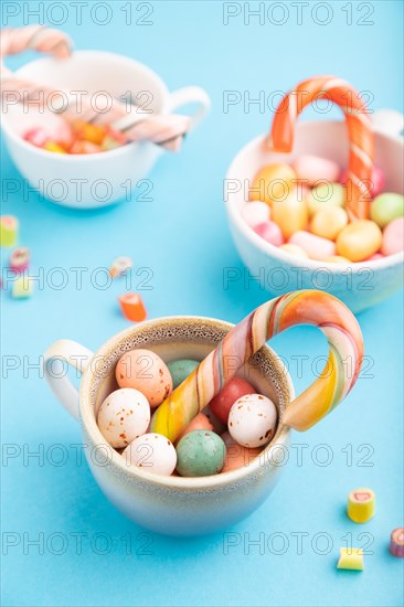 Heap of multicolored caramel candies in cups on blue pastel background. close up, side view,