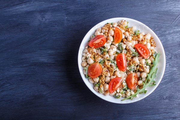 Vegetarian salad of boiled chickpeas, cheese, arugula, mustard and cherry tomatoes on black wooden