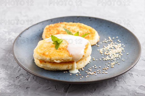Cheese pancakes on a blue ceramic plate with milk sauce on a gray concrete background. side view,