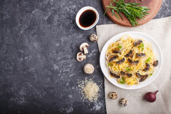 Rice noodles with champignons mushrooms, egg sauce and oregano on white ceramic plate on a black