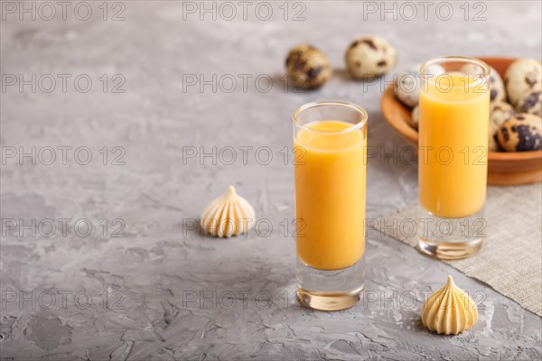 Sweet egg liqueur in glass with quail eggs and meringues on a gray concrete background. Side view,