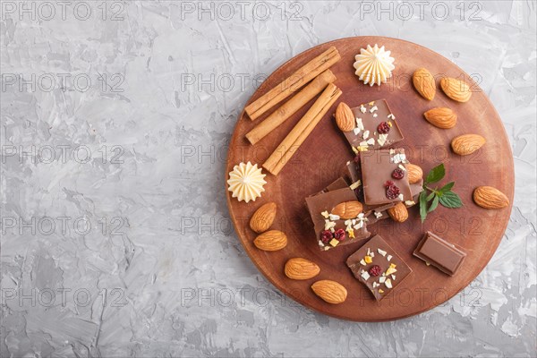 A pieces of milk chocolate with almonds and dried fruits on a brown wooden board on a gray concrete