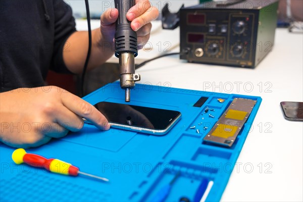 Close-up of a unrecognizable male technician fixing a mobile phone using a soldering iron in a