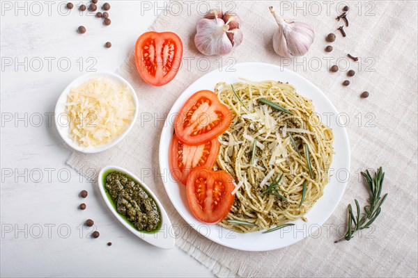 Spaghetti pasta with pesto sauce, tomatoes and cheese on a linen tablecloth on white wooden
