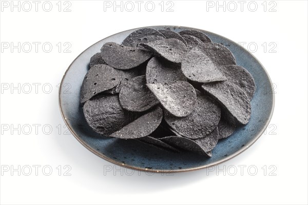 Black potato chips with charcoal on a blue ceramic plate isolated on white background. side view,