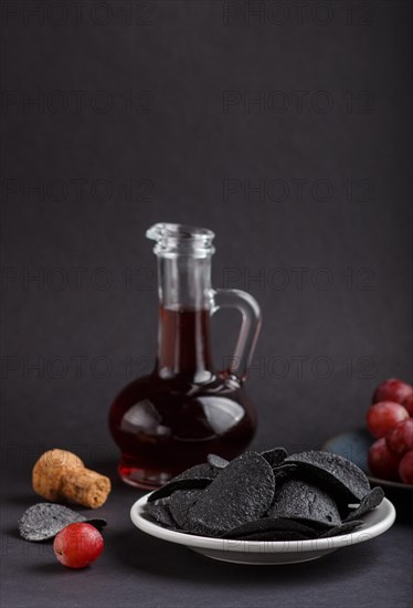 Black potato chips with charcoal, balsamic vinegar in glass, red grapes on a blue ceramic plate on