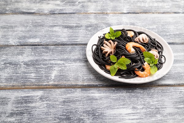 Black cuttlefish ink pasta with shrimps or prawns and small octopuses on gray wooden background.