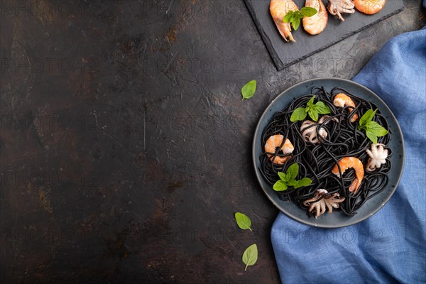 Black cuttlefish ink pasta with shrimps or prawns and small octopuses on black concrete background