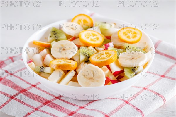 Vegetarian salad of bananas, apples, pears, kumquats and kiwi on linen tablecloth, close up,