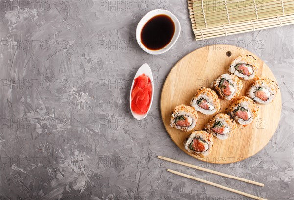 Japanese maki sushi rolls with salmon, sesame, chopsticks, soy sauce and marinated ginger on wooden