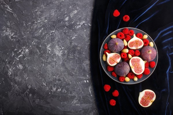 Fresh figs, strawberries and raspberries on blue ceramic plate on black concrete background and