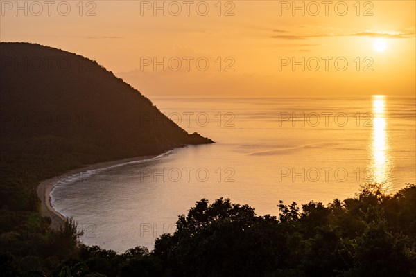 View from a mountain to a secluded bay with a sandy beach and mangrove forest. The sun rises over